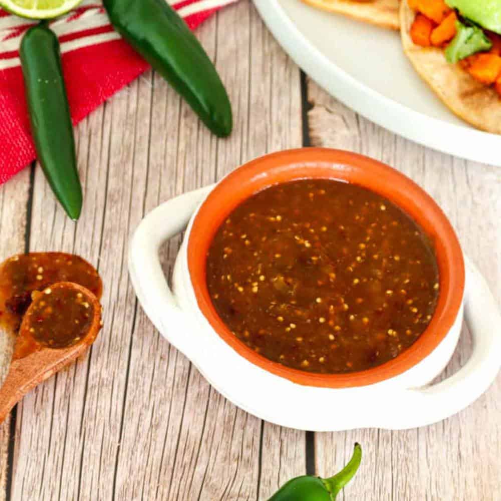 Chile morita salsa in a white bowl. Two sweet potato tacos in the upper right corner.