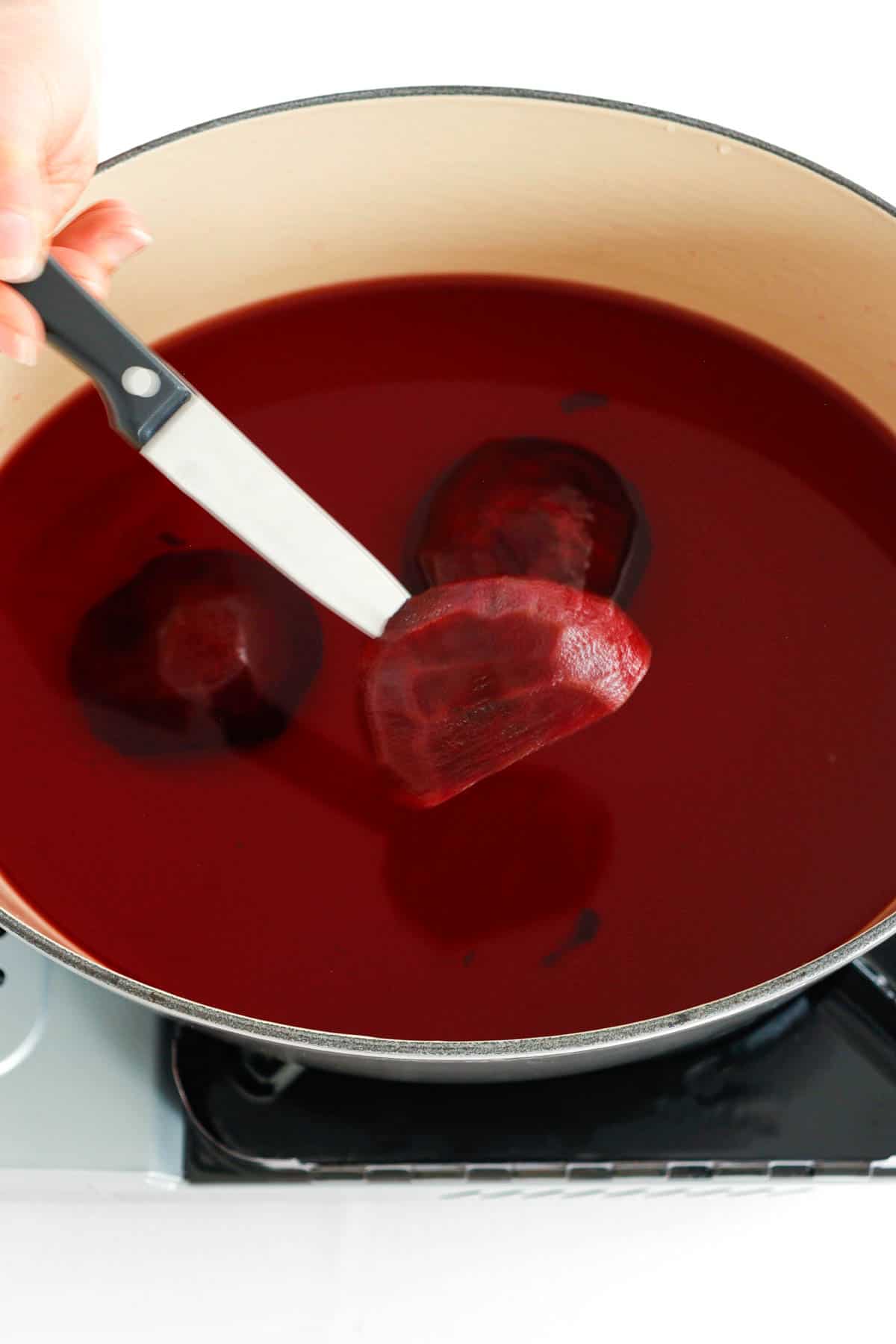 Beets been cooked in a pot. A pairing knife piercing through one of the beets.