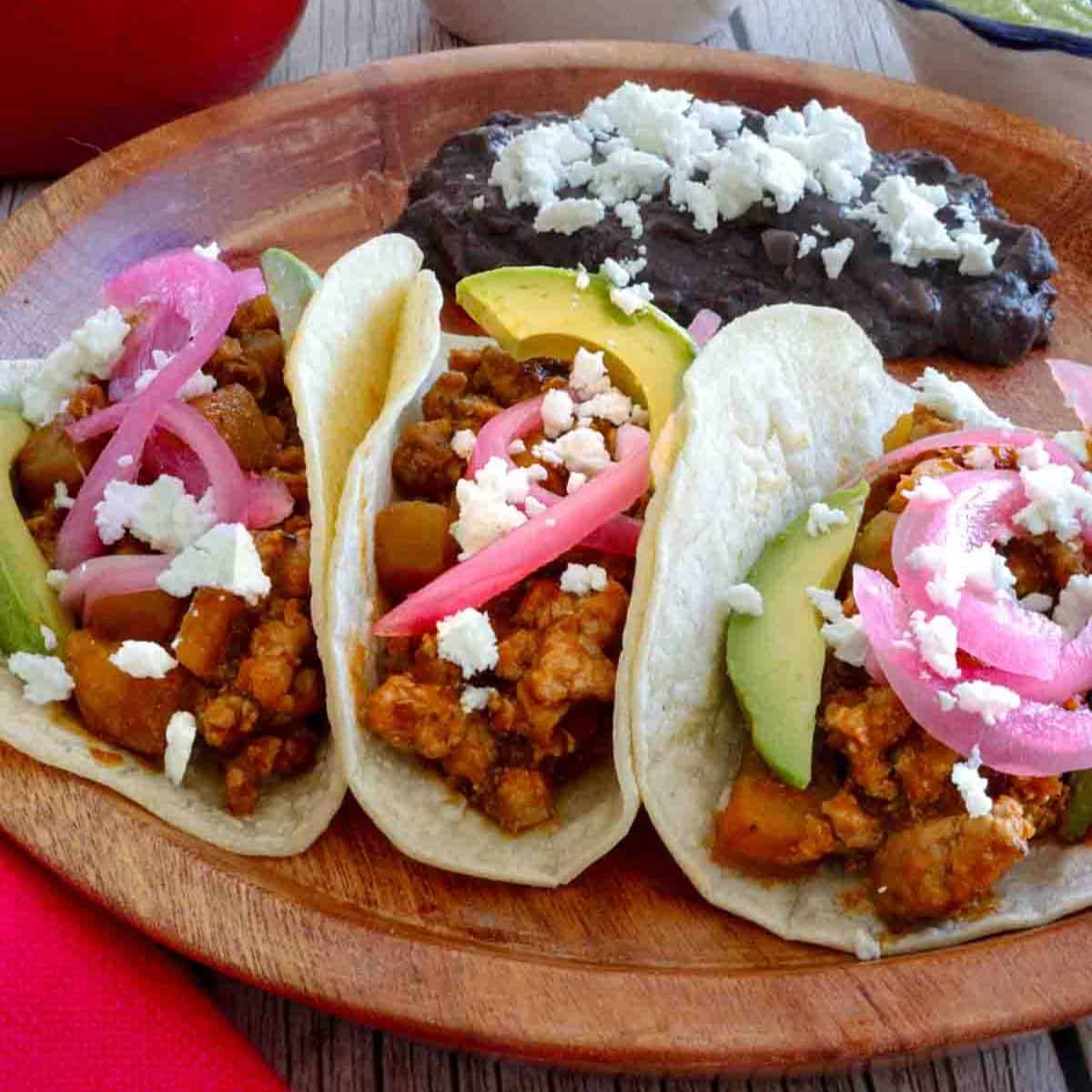 Ground pork tacos Mexican recipe - three pork tacos with red pickled onions and fried beans.