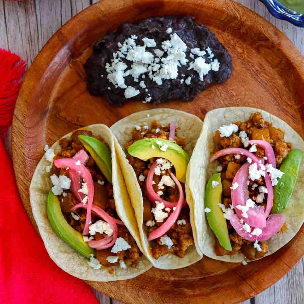 Three ground pork tacos with red pickled onions, avocado and salsa.