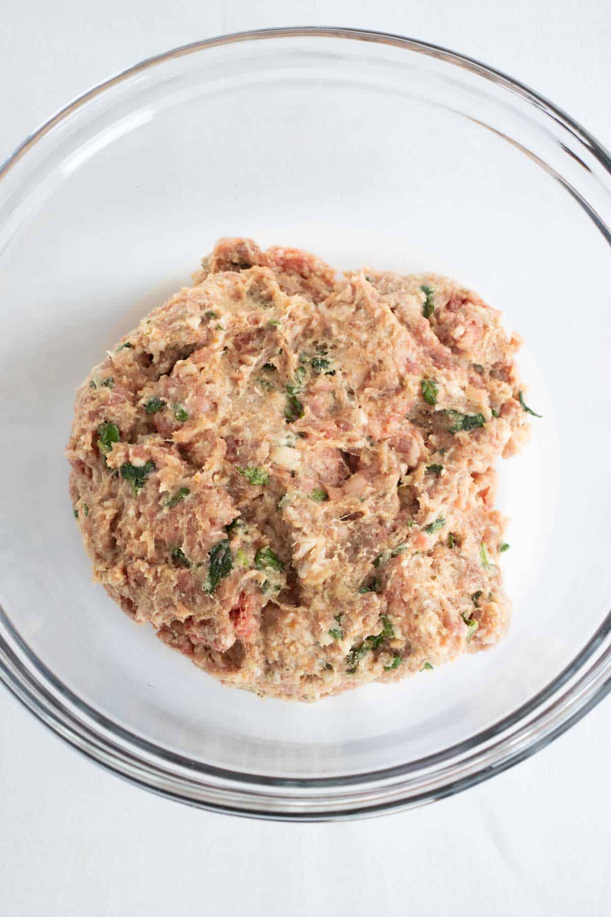 Ground pork and beef mixed up in bowl to prepare Baked Mexican Meatballs with sauce.