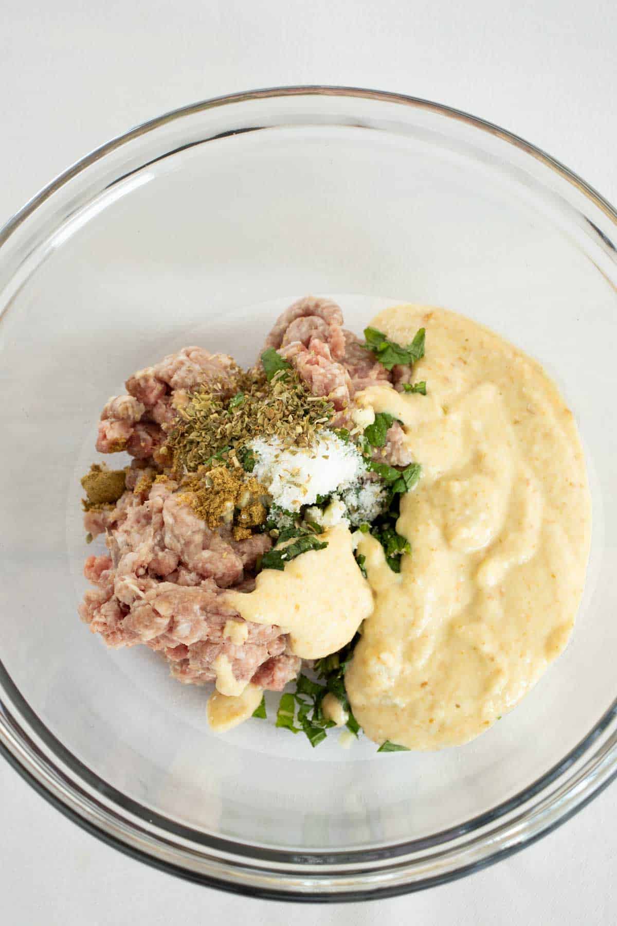 Ground Pork and other ingredients in bowl for preparing Baked Mexican Meatballs in sauce