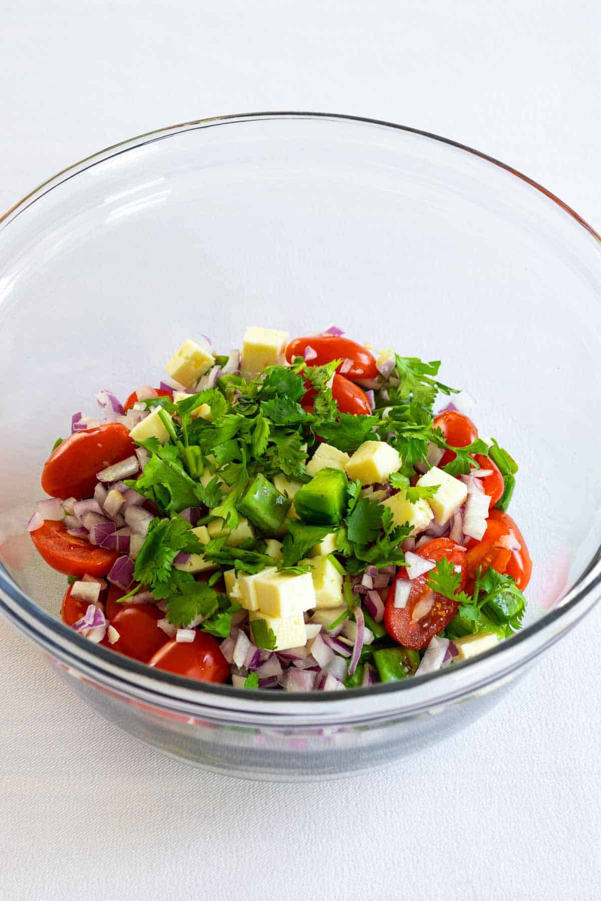 Cherry tomatoes, onion, feta cheese, cilantro, and nopales in a bowl ready for tossing.