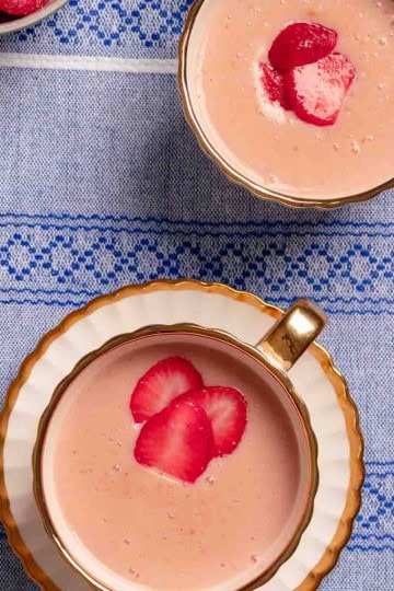 Strawberry atole served in two mugs. There are some frozen strawberries on the corner.