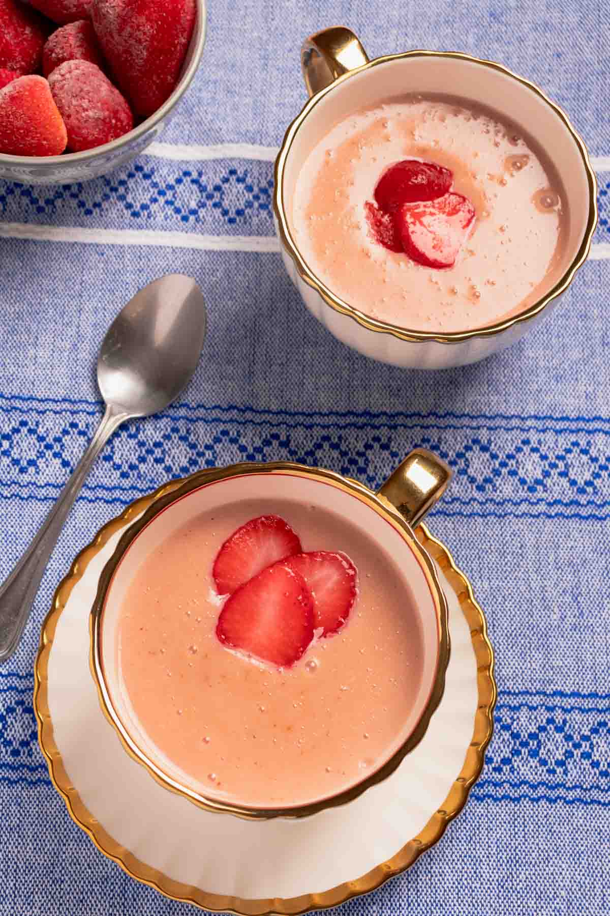 Strawberry atole served in two mugs. There are some frozen strawberries on the corner.
