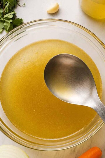 Chicken broth served in a transparent bowl and some of the ingredients to make it are in the picture.