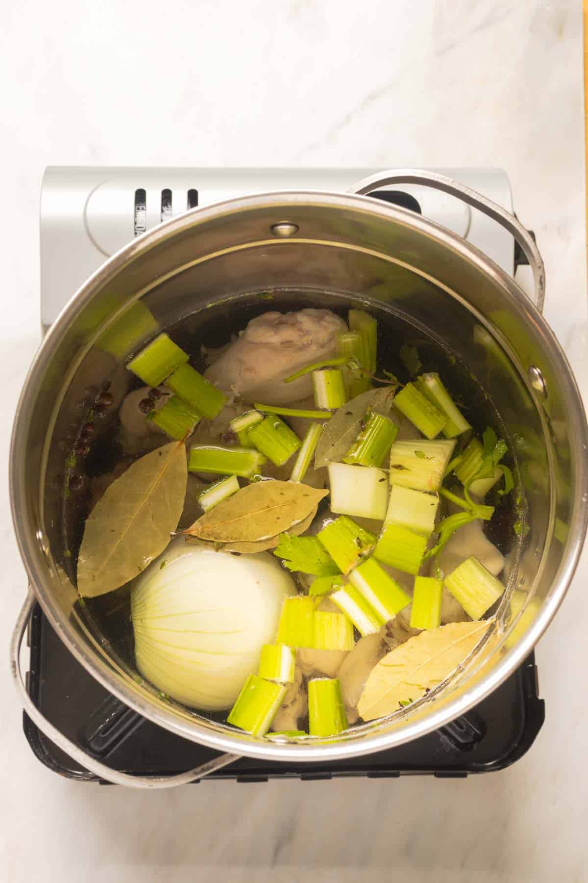 Chicken, herbs and aromatics starting to get cooked in a pot.