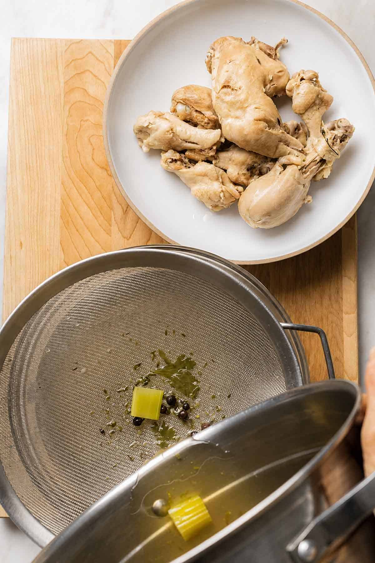 Cooked chicken removed from the pot and using the colander to remove the solids.
